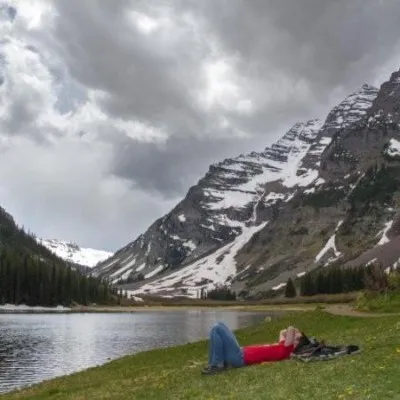Kyle lying in the grass beside a lake, snow-covered mountains behind.
